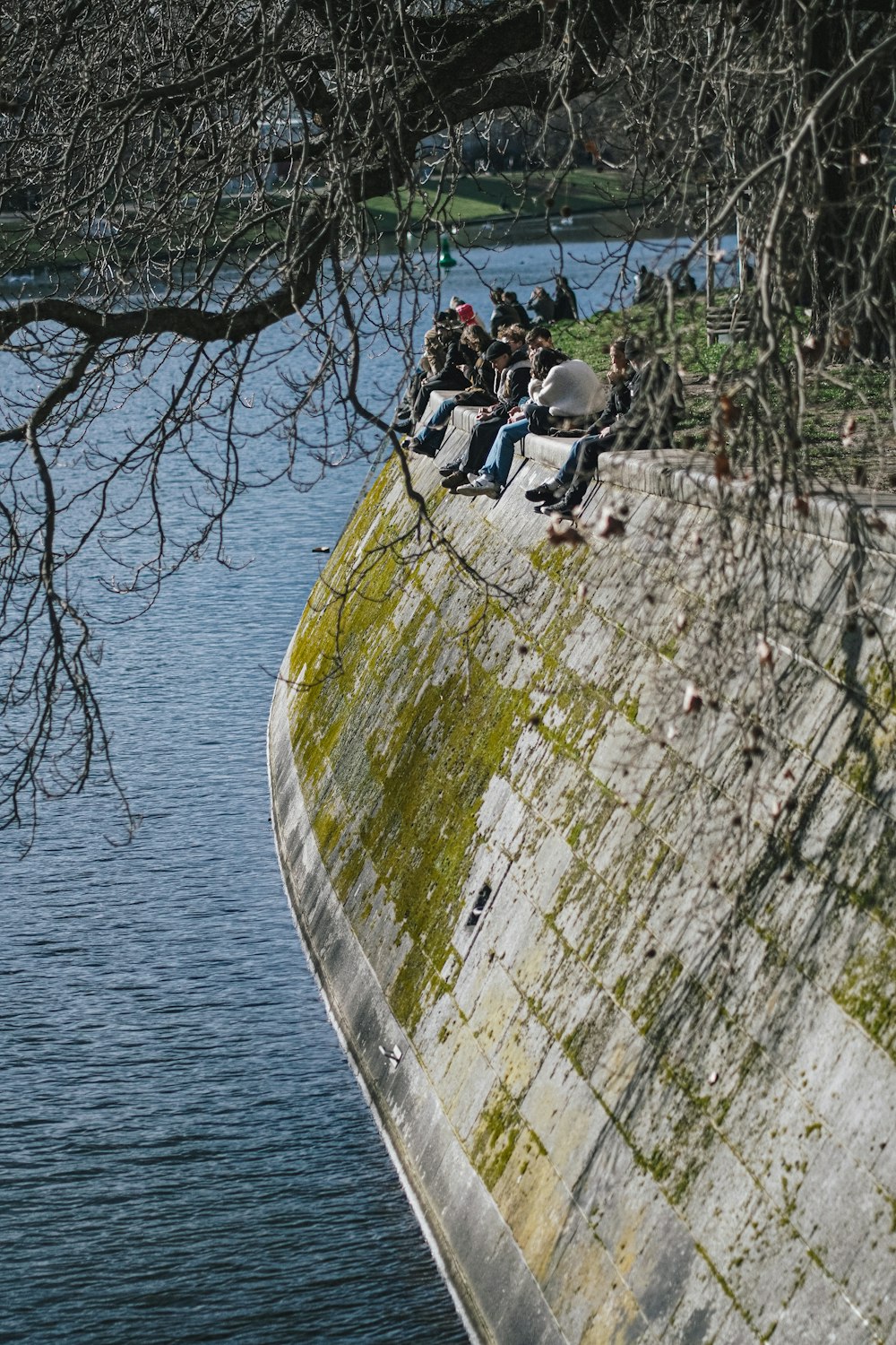 a group of people sitting on top of a cement wall next to a body of