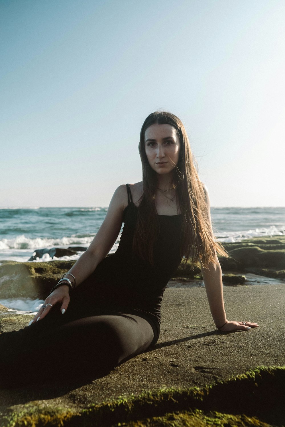 a woman sitting on the beach with her legs crossed