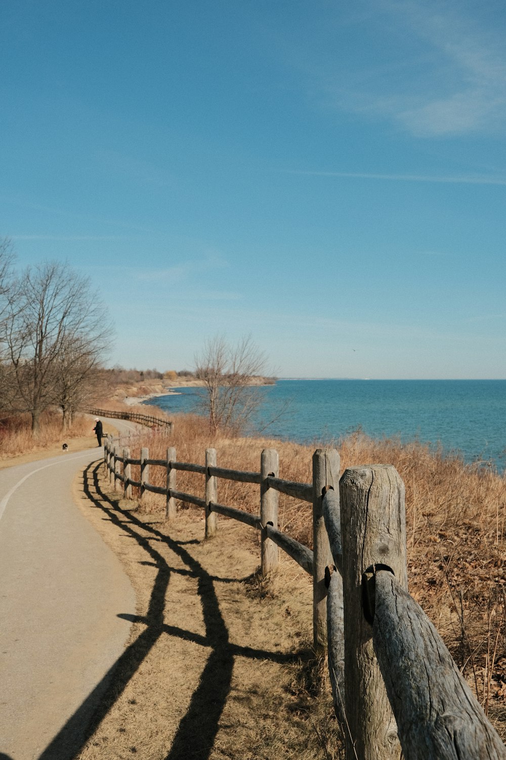 a wooden fence along the side of a road next to a body of water