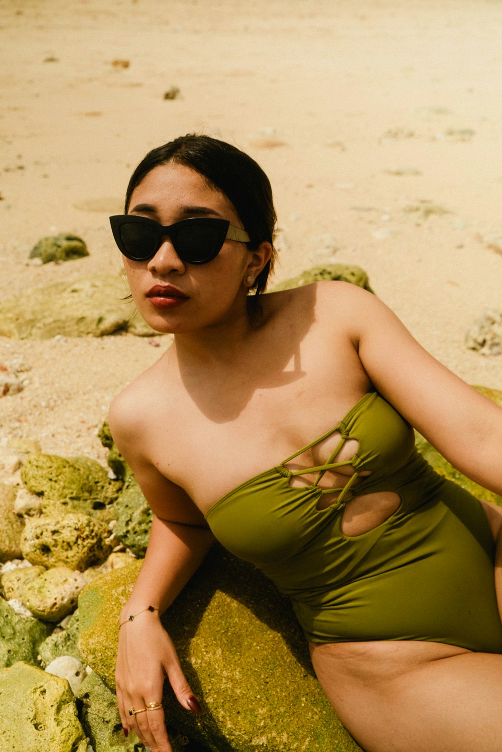 a woman in a green swimsuit sitting on a rock