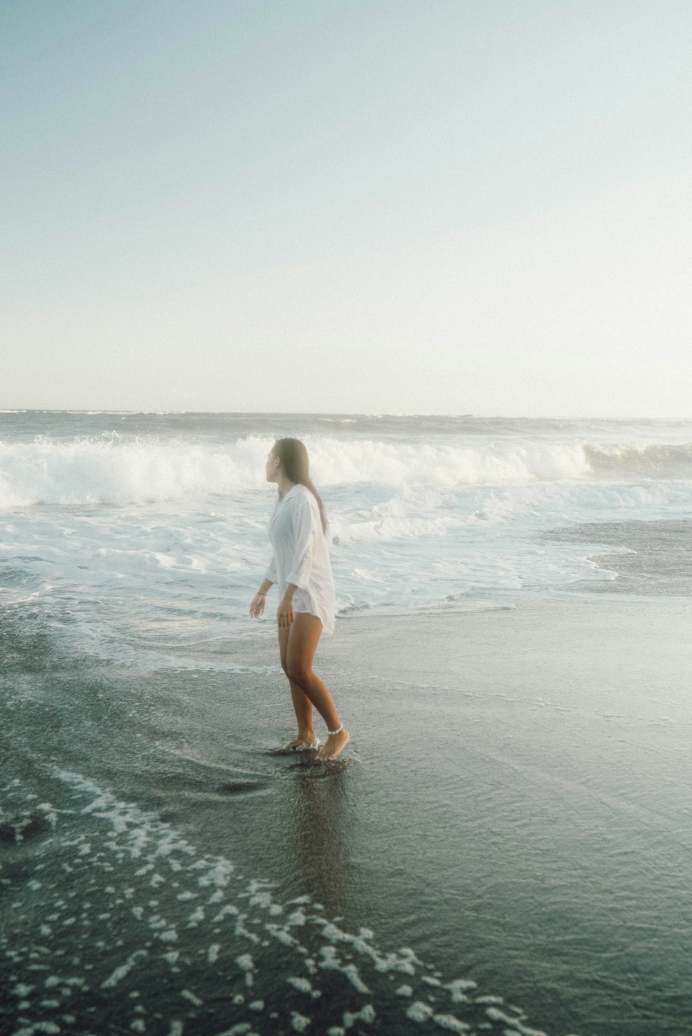 a woman walking along a beach next to the ocean