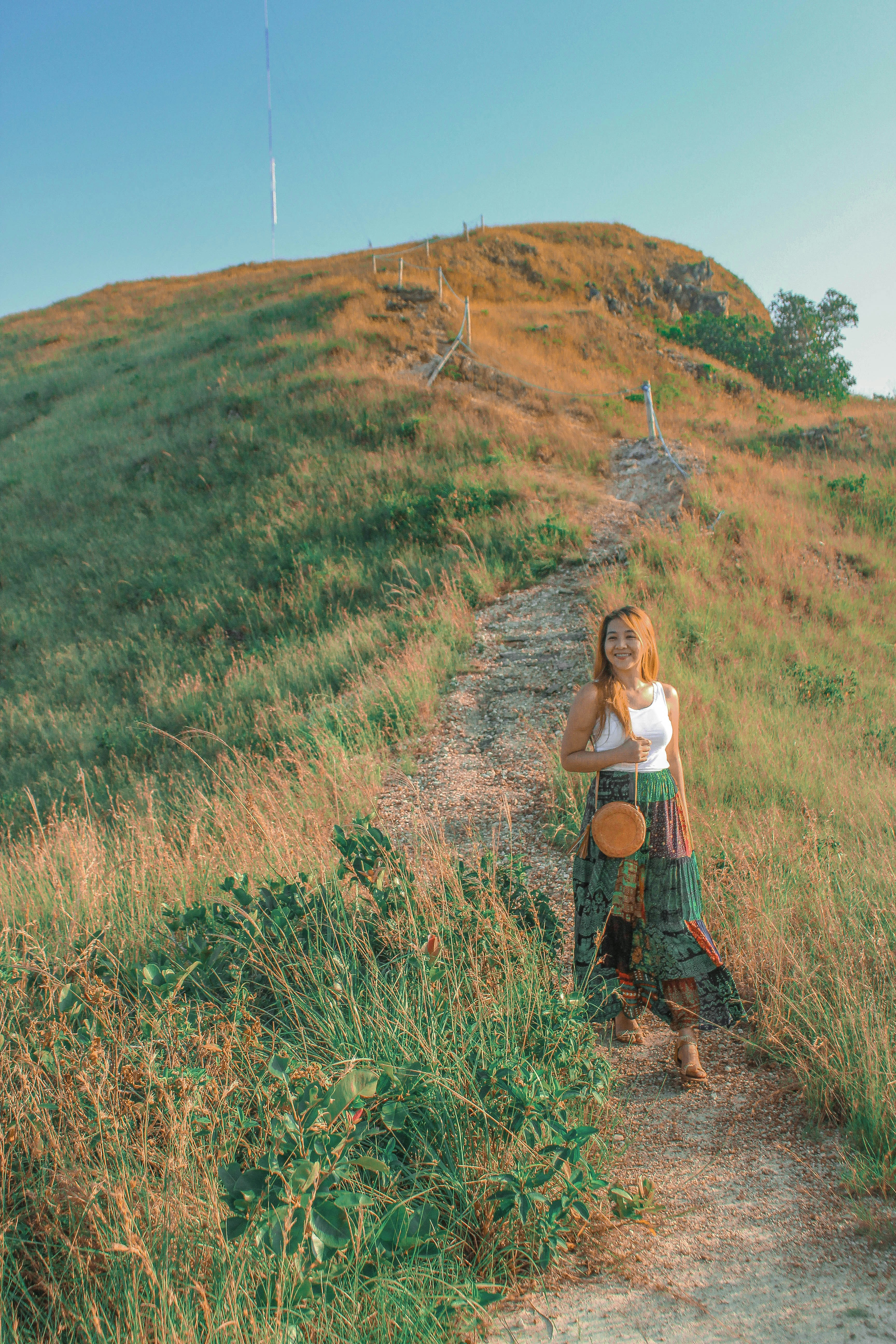 una donna in piedi su un sentiero sterrato vicino a una collina erbosa