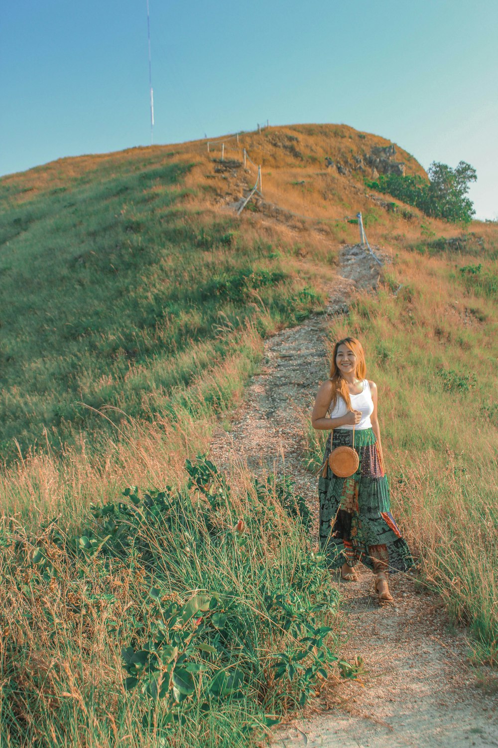 a woman standing on a dirt path near a grassy hill