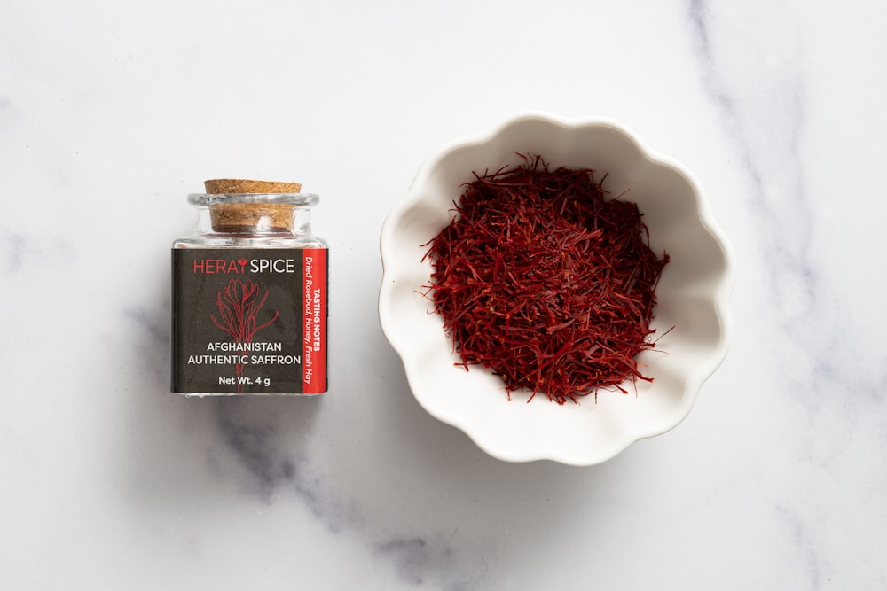 a bowl of red saffron seeds next to a bottle of red spice