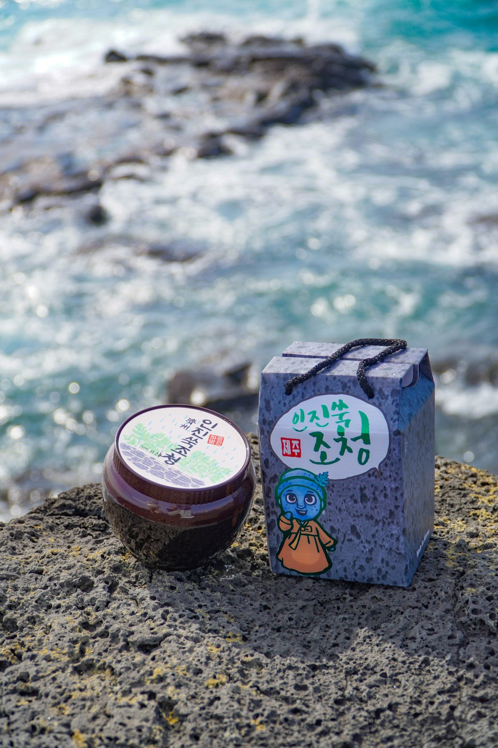 a container of jam sitting on top of a rock next to the ocean