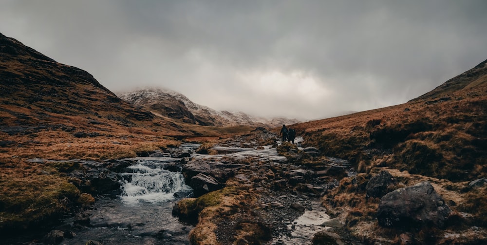 a man walking across a stream in the mountains