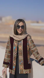 a woman wearing sunglasses and a scarf standing next to a wall