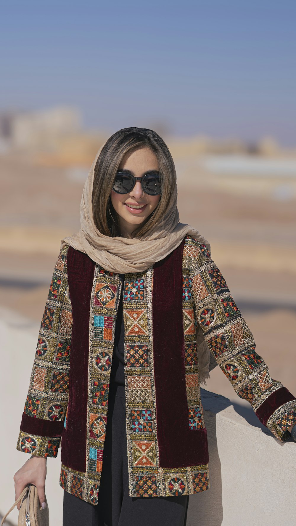 a woman wearing sunglasses and a scarf standing next to a wall