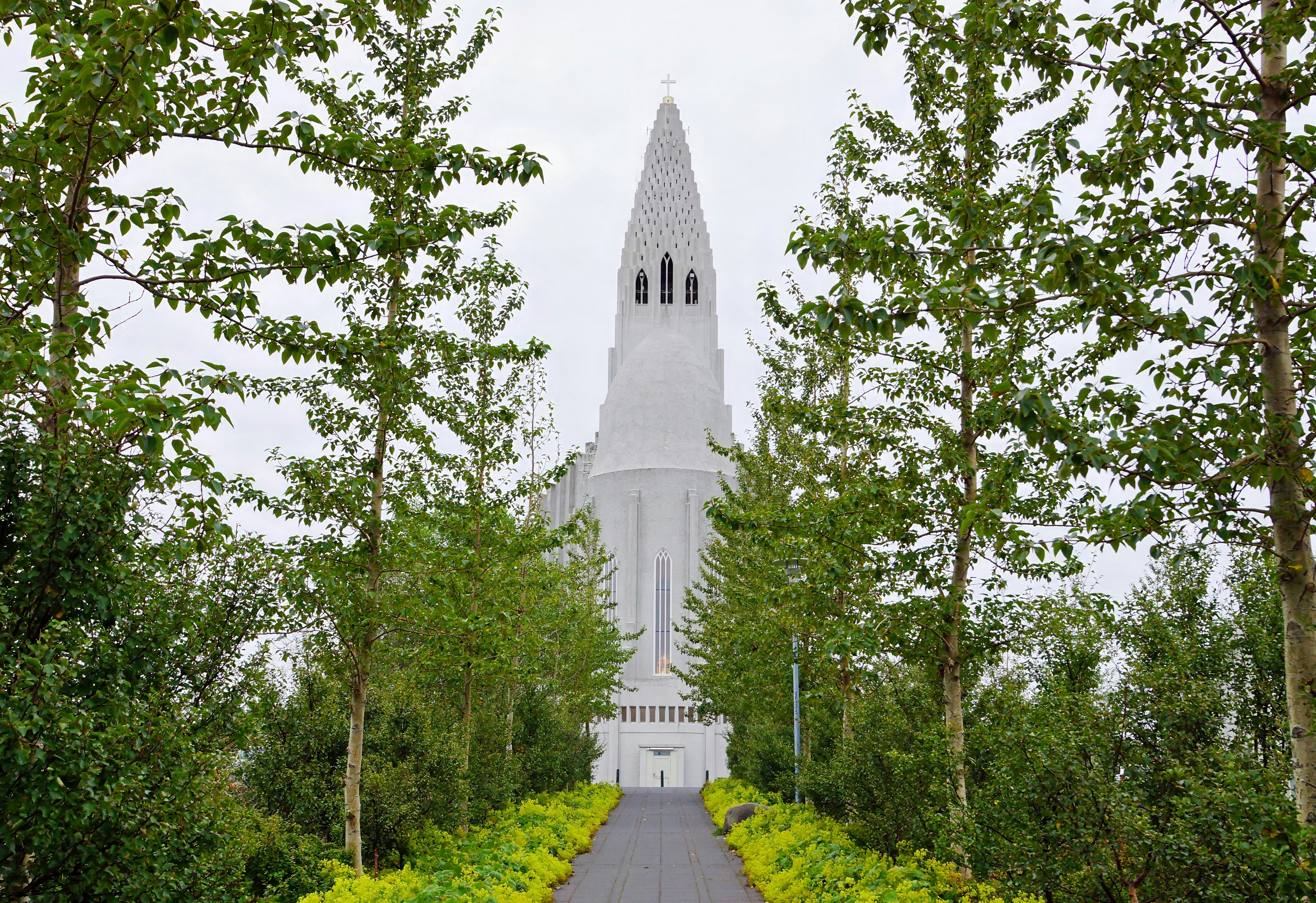  An image of Hallgrimskirkja church surrounded by trees and a pathway leading up to its entrance.