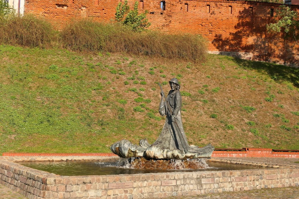 eine Statue einer Frau, die neben einem Brunnen steht