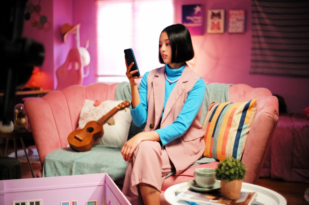 une femme assise sur un canapé rose tenant un téléphone portable