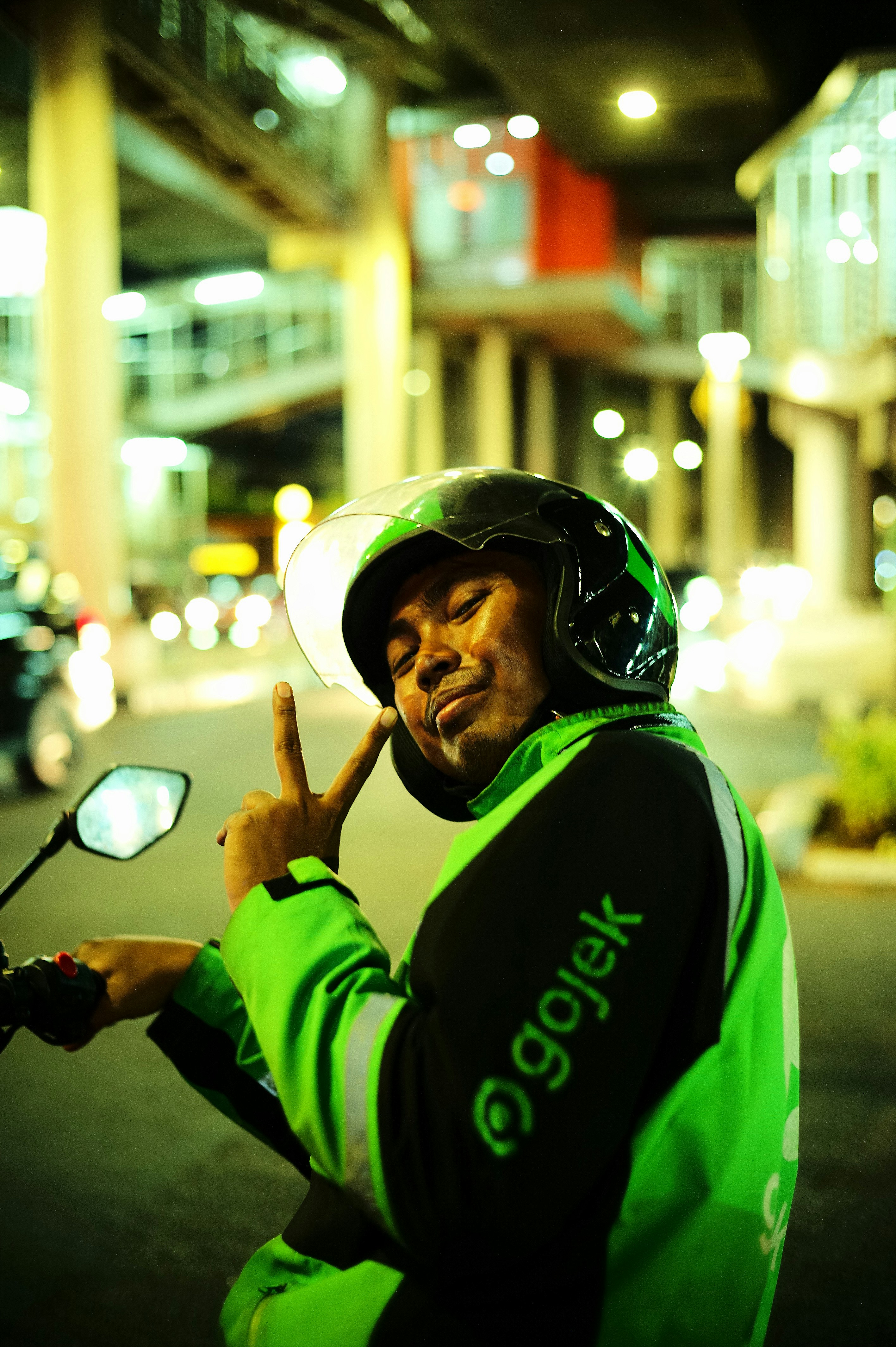 Seorang pria berjaket hijau di atas sepeda motor memberikan tanda perdamaian