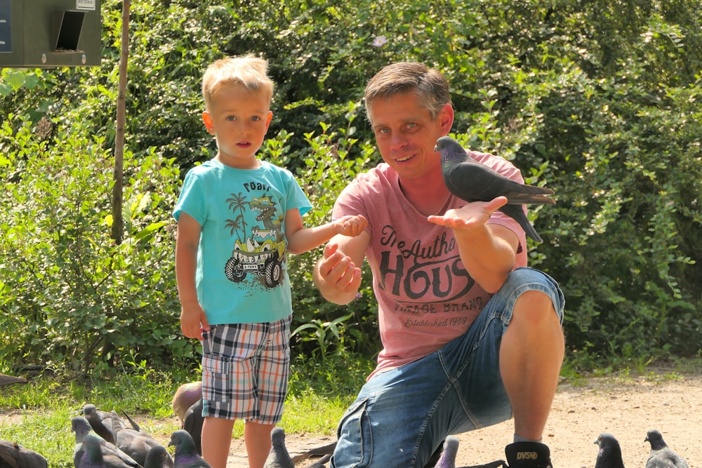 a man kneeling down next to a little boy near a flock of birds