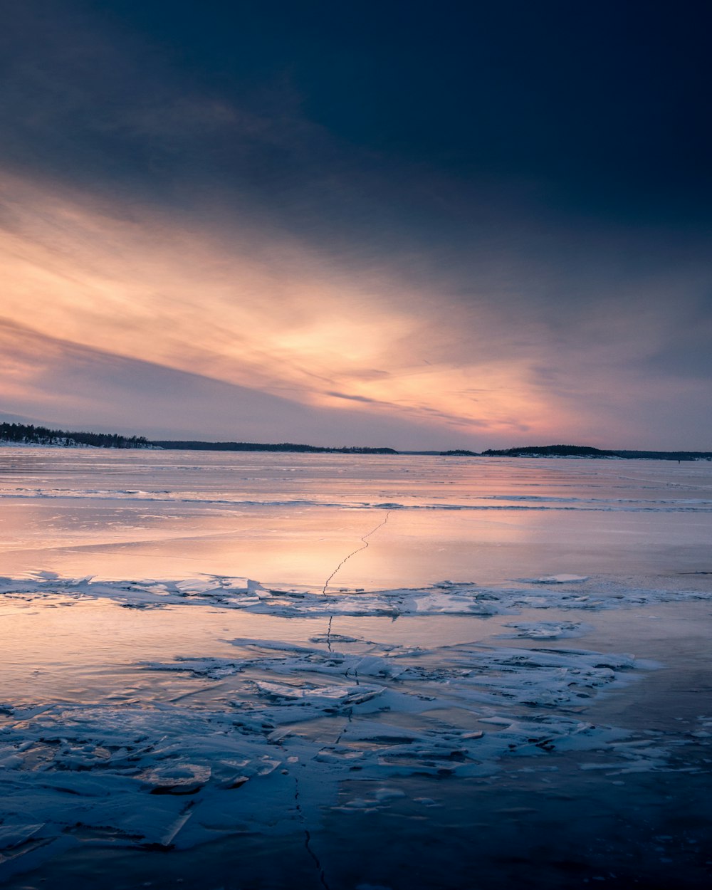 a man fishing on a frozen lake at sunset
