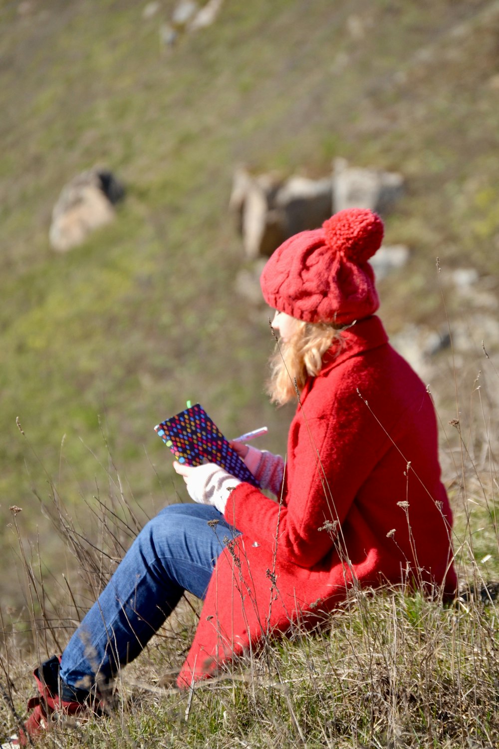 a woman in a red coat is sitting on a hill