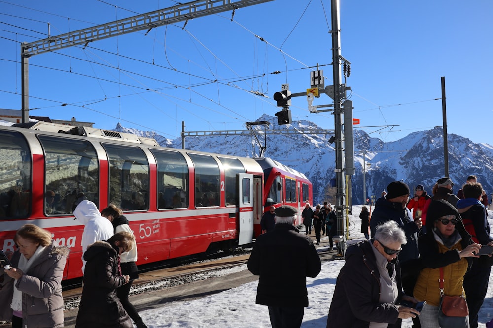 a group of people standing next to a red and white train