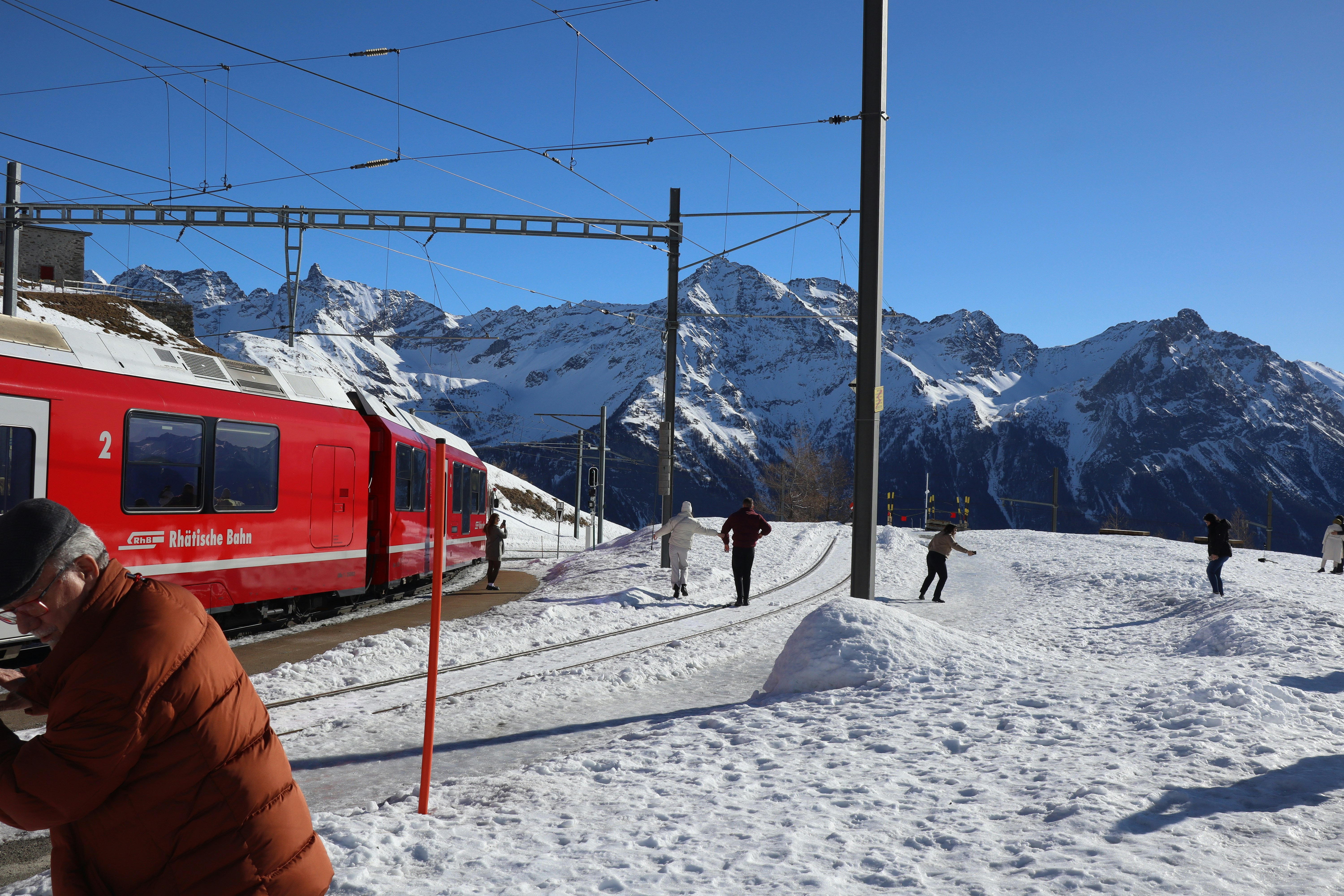 a red train traveling down train tracks next to snow covered mountains, 