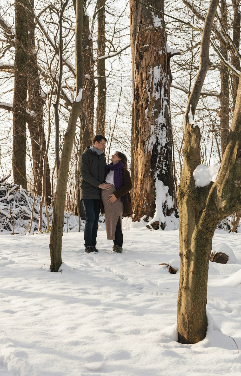 a man and woman standing in the snow next to a tree