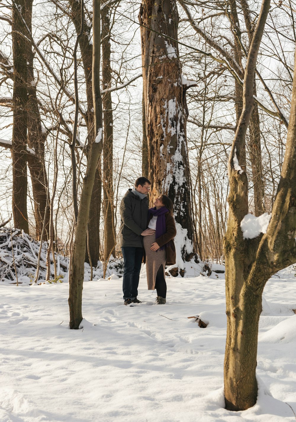 a man and woman standing next to a tree in the snow