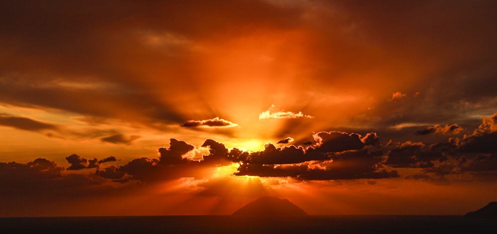 the sun is setting over a mountain with clouds