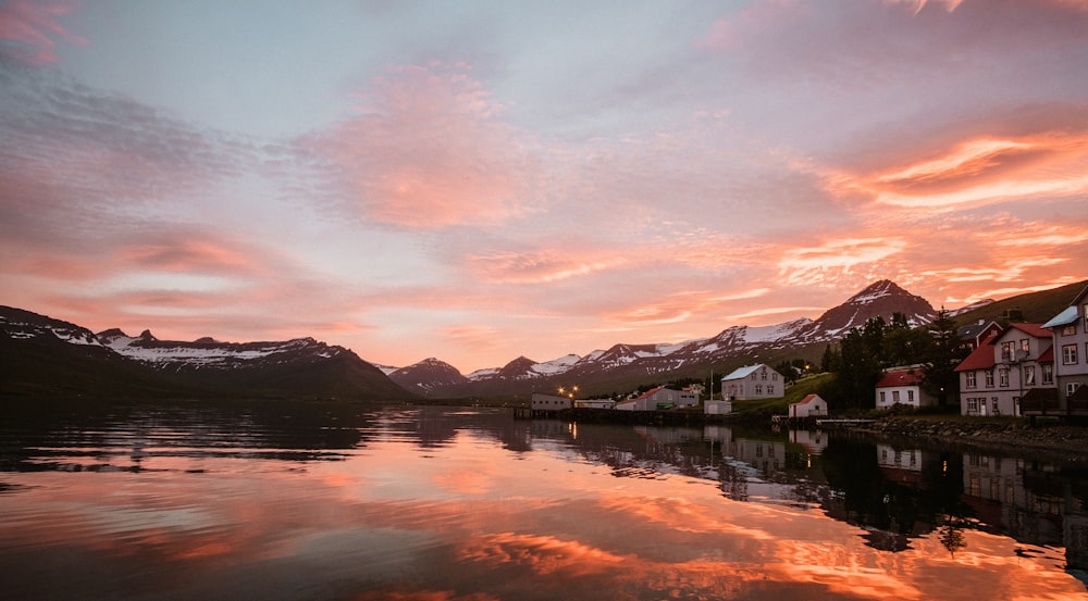 a lake with houses and mountains in the background