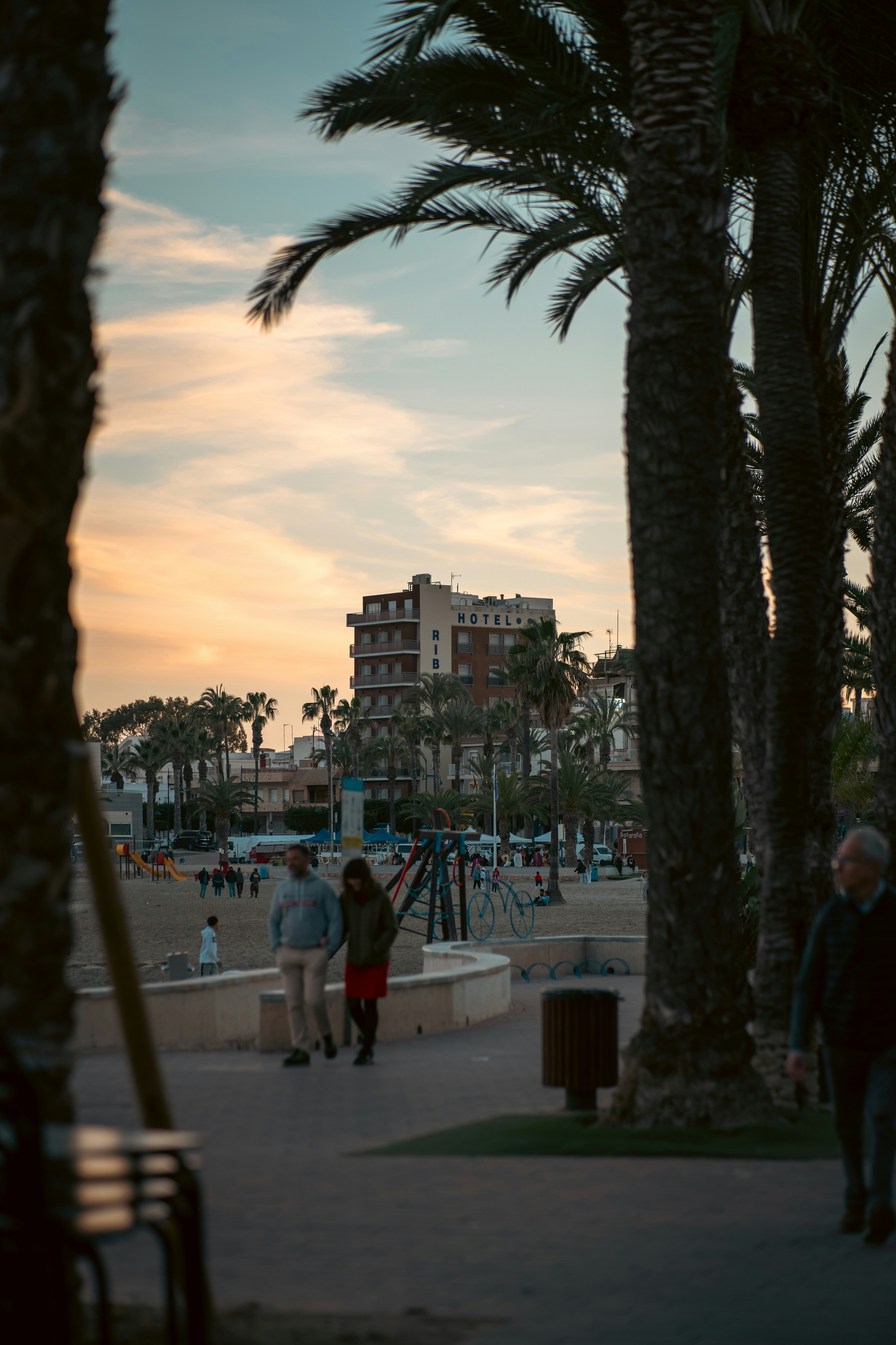 a group of people walking down a sidewalk next to palm trees