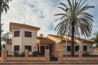 a house with a fence and palm trees in front of it