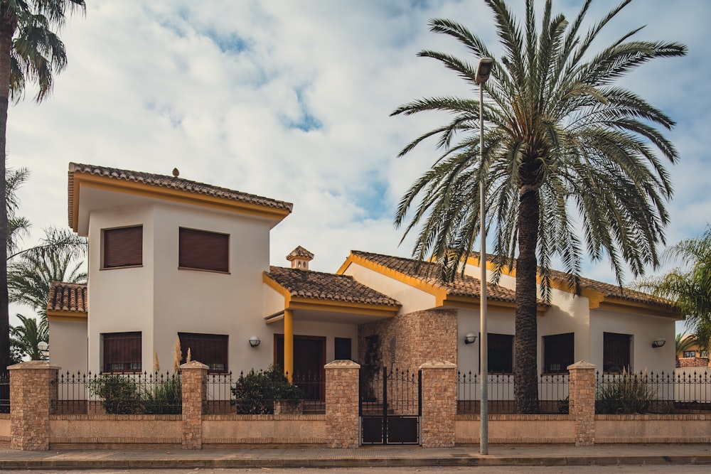 a house with a fence and palm trees in front of it