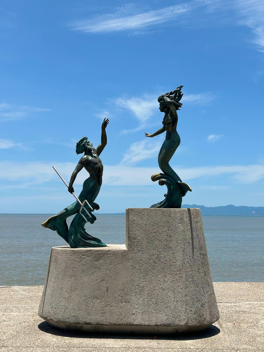 a statue of two mermaids on a rock near the ocean