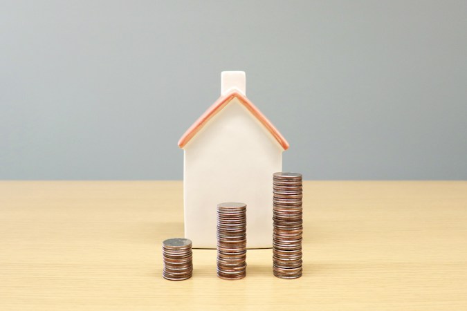 A small house model next to stacks of coins representing home equity and monthly costs