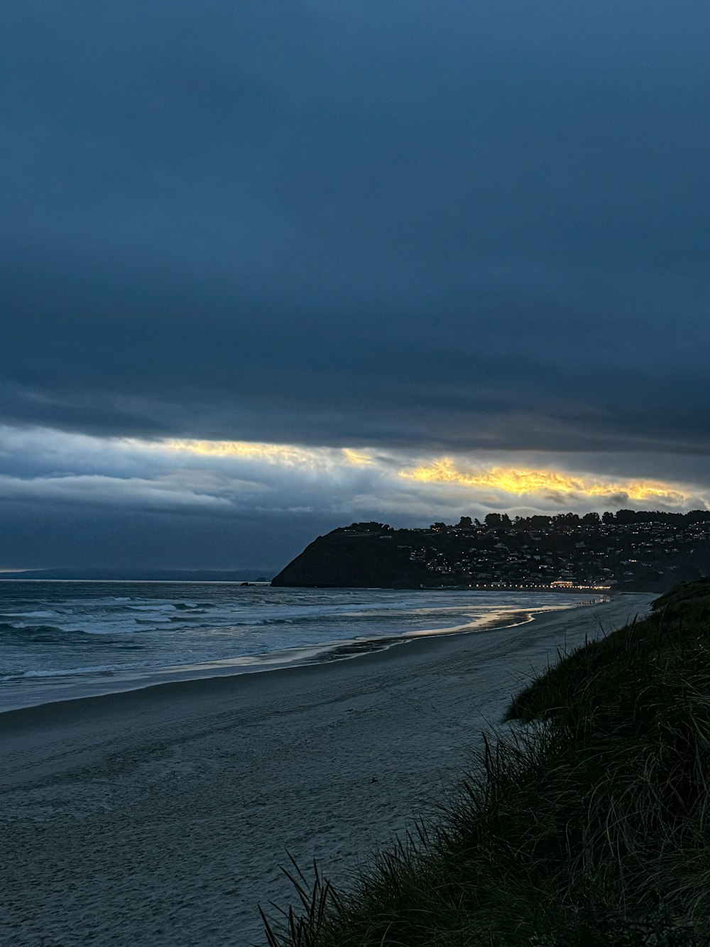 a bench sitting on top of a sandy beach under a cloudy sky