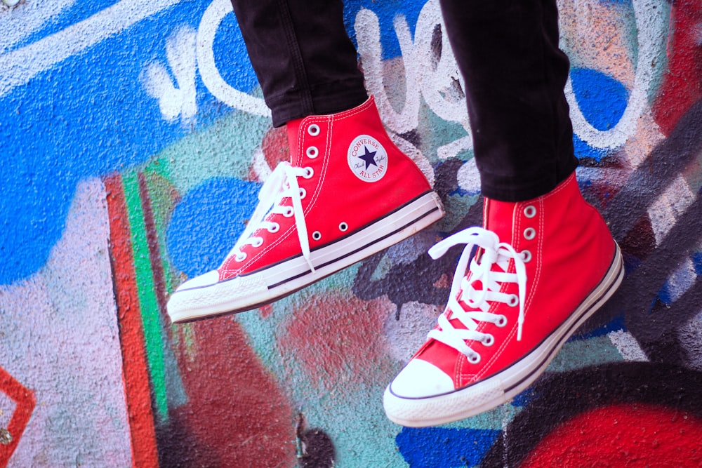 a person wearing red converse shoes standing on a graffiti covered wall