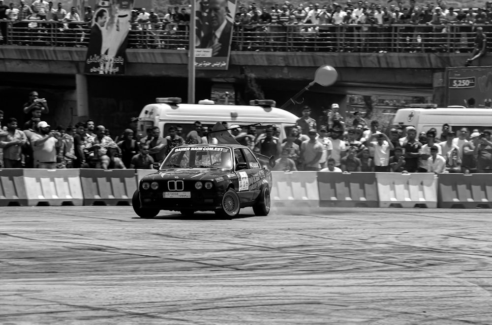 a man driving a small car in front of a crowd of people