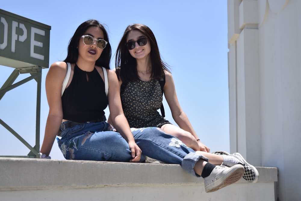 two women sitting on a ledge with a sign in the background