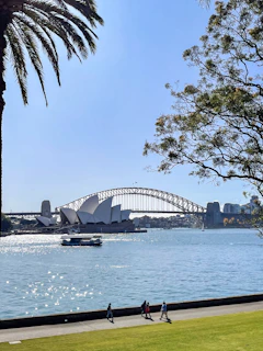 people walking on a path near the water with a bridge in the background