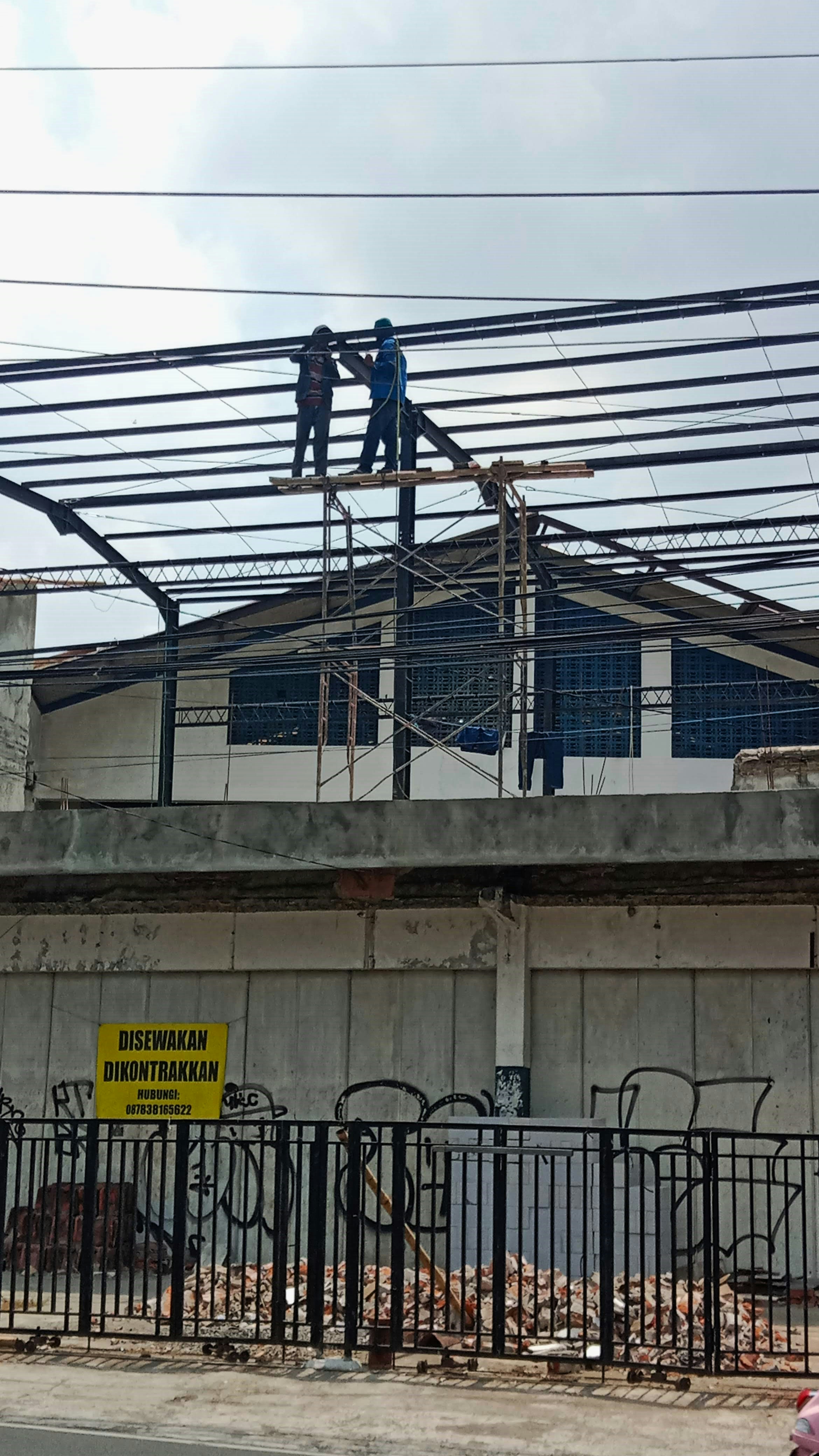 Commercial shopping centre under construction with structural steel framework and workers installing roof beams, bright industrial setting