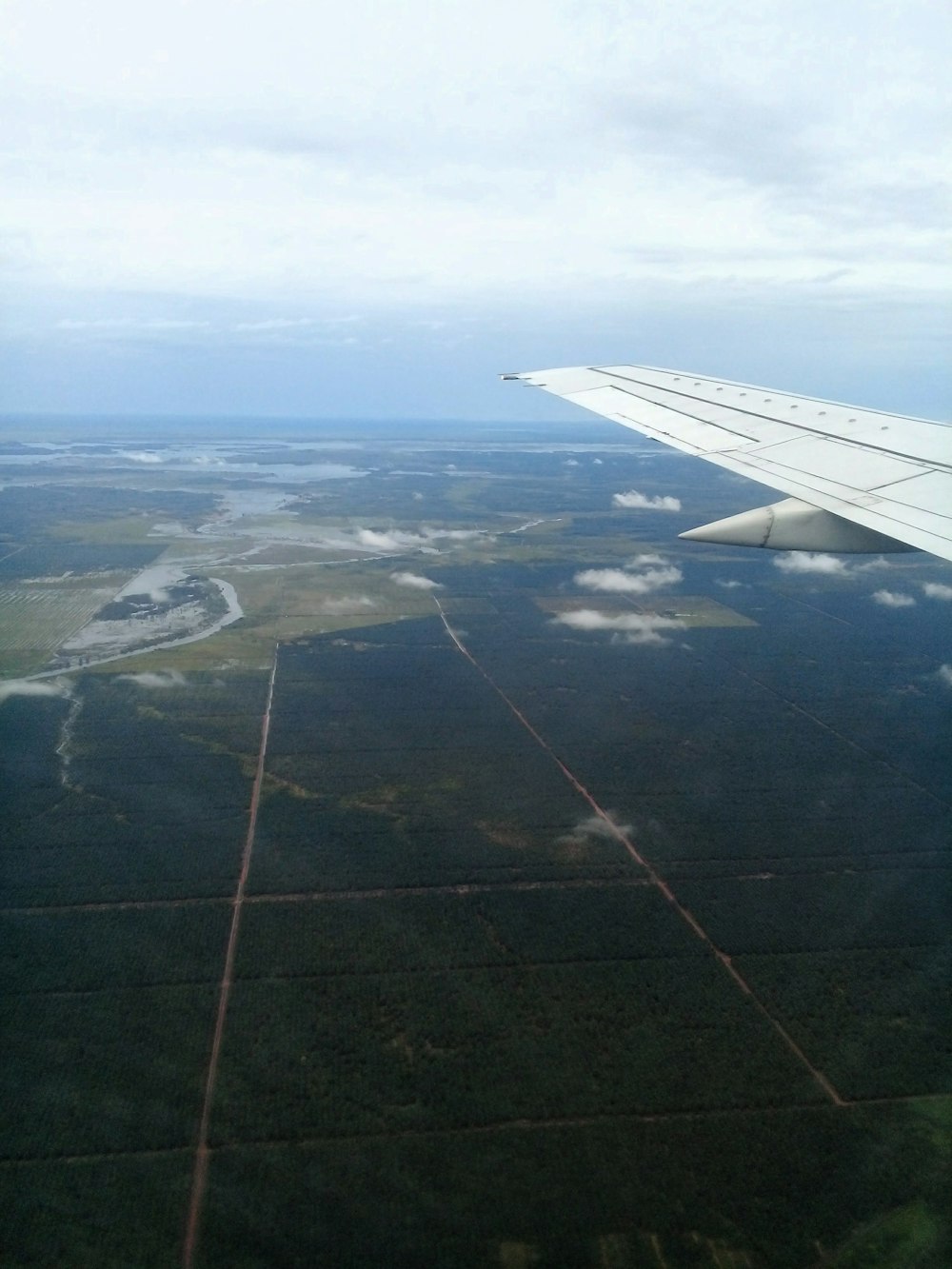 the wing of an airplane flying over a lush green field