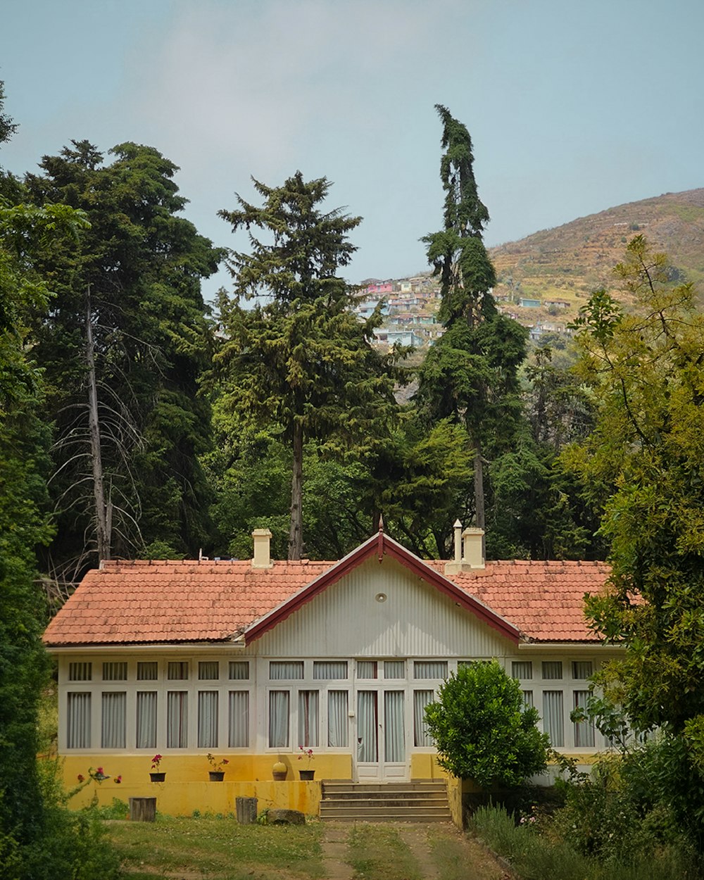 a yellow house with a red roof surrounded by trees