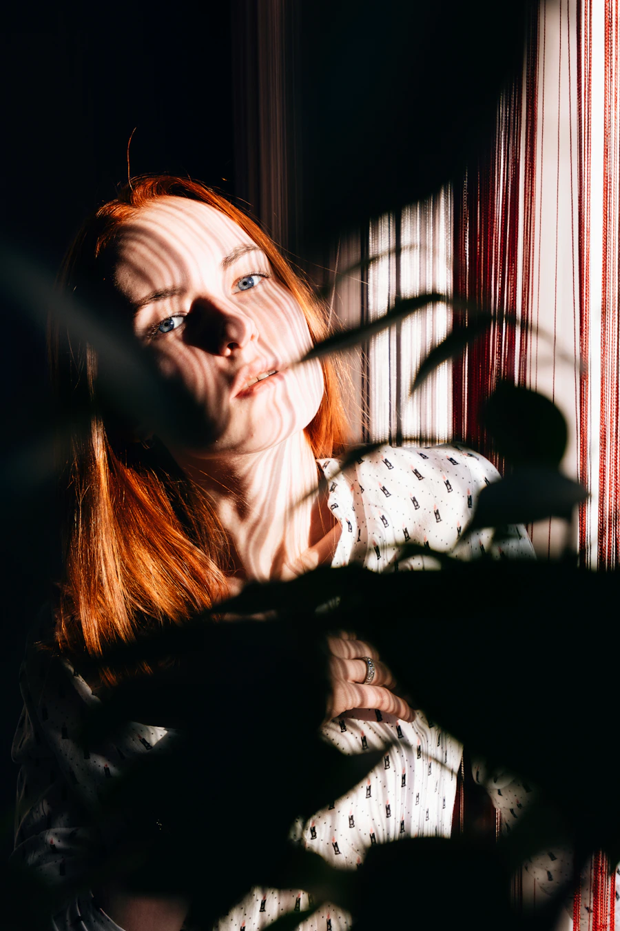 Red-haired woman in a white shirt, softly lit by a nearby window