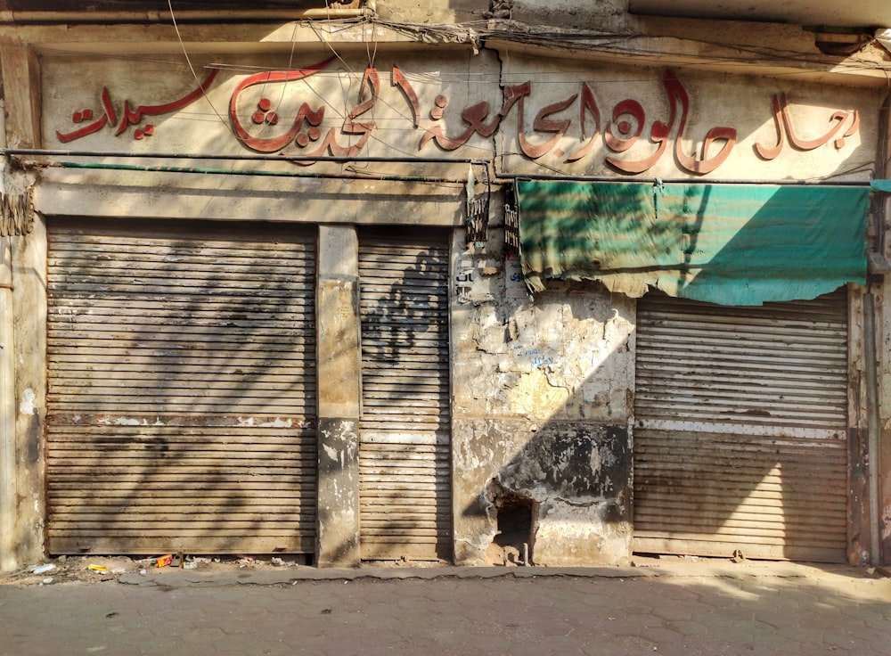 a run down building with closed shutters and graffiti on it