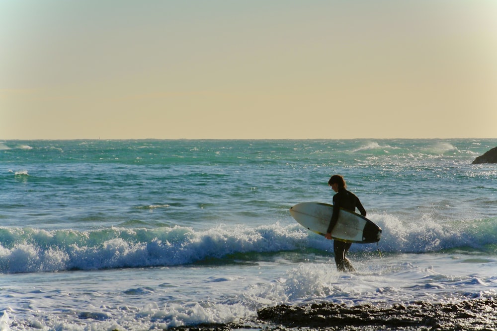 a man holding a surfboard walking into the ocean