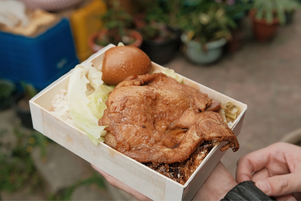 a person holding a box of food with a chicken in it