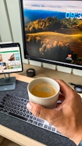 uma pessoa segurando uma xícara de café em frente a um computador