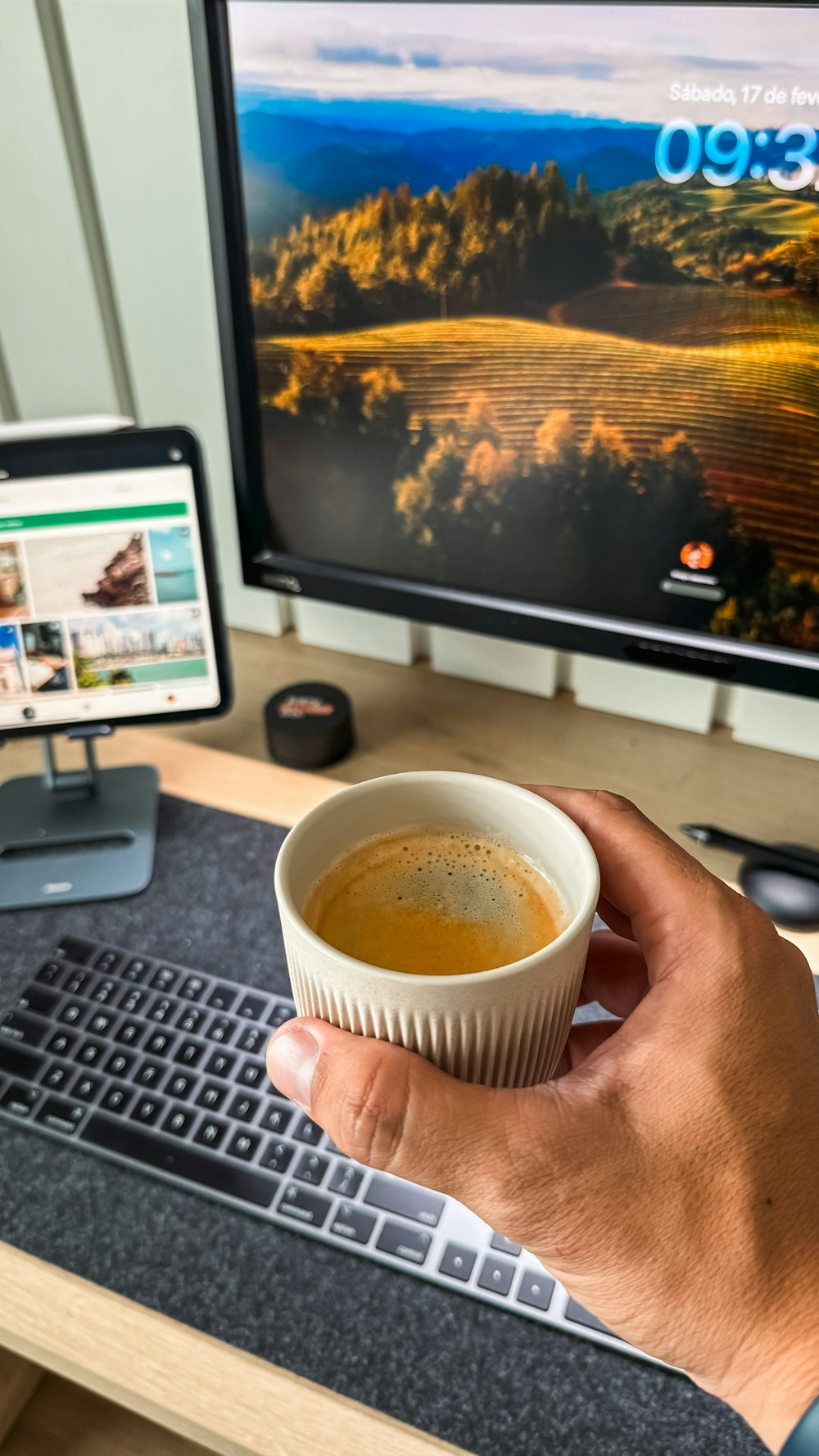 a person holding a cup of coffee in front of a computer