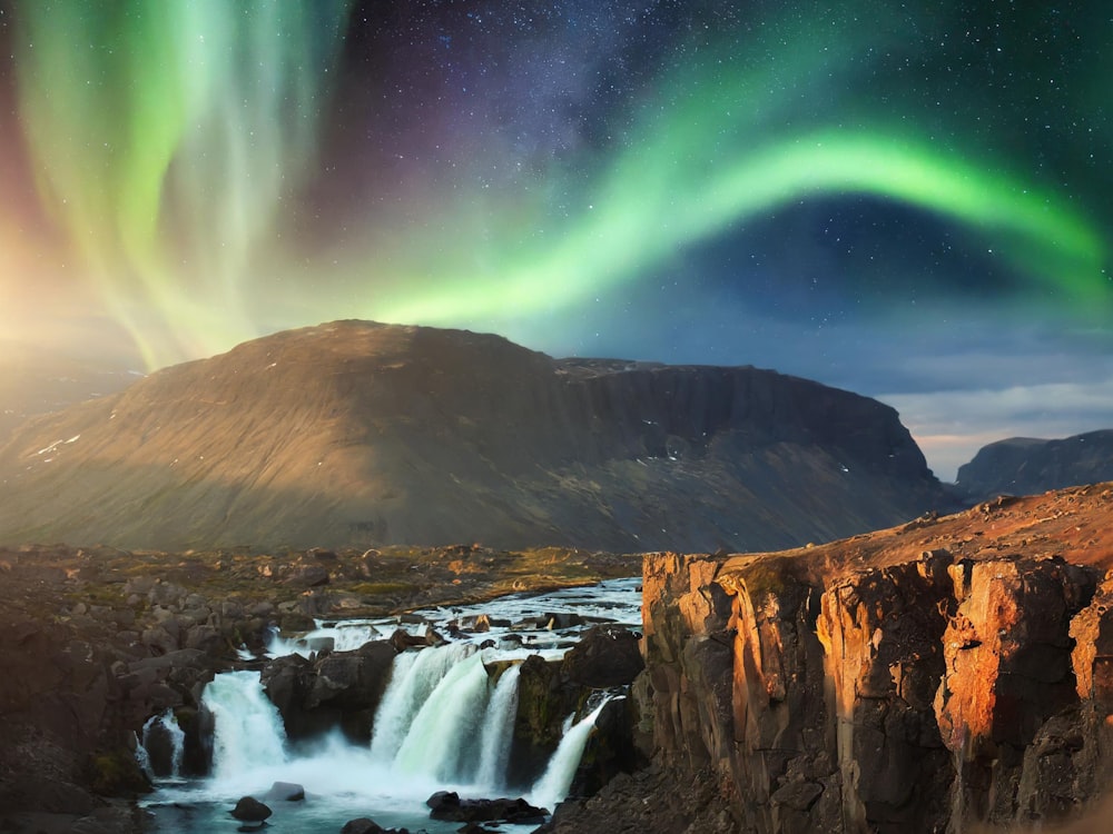 a waterfall with a green and purple aurora light above it