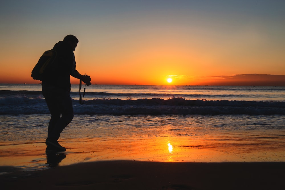 a man walking on the beach at sunset