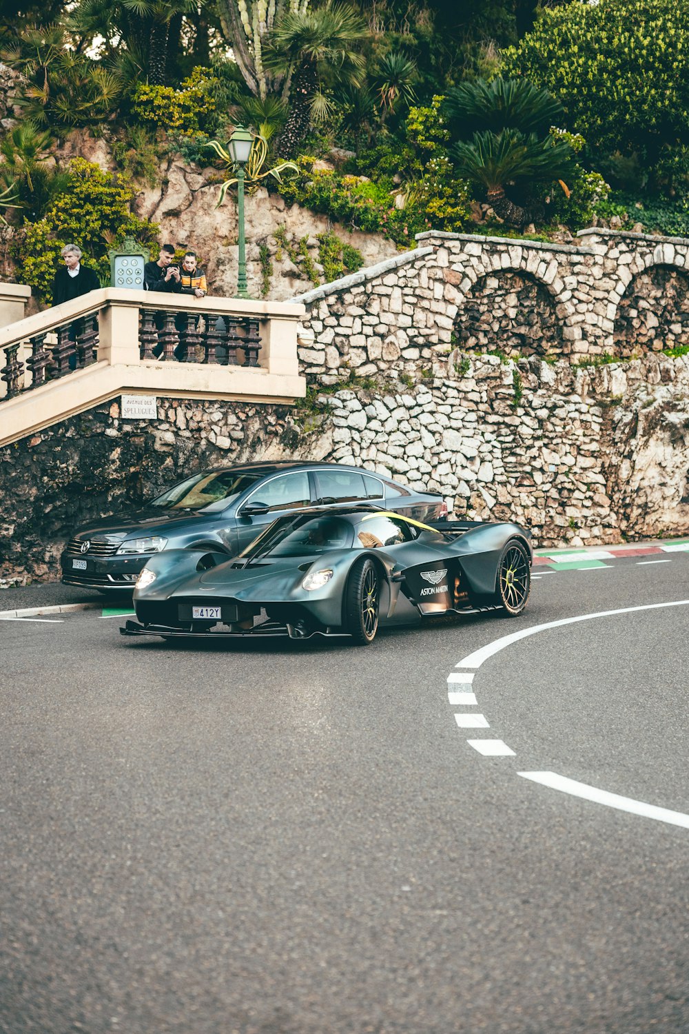 a black sports car driving down a street next to a stone wall