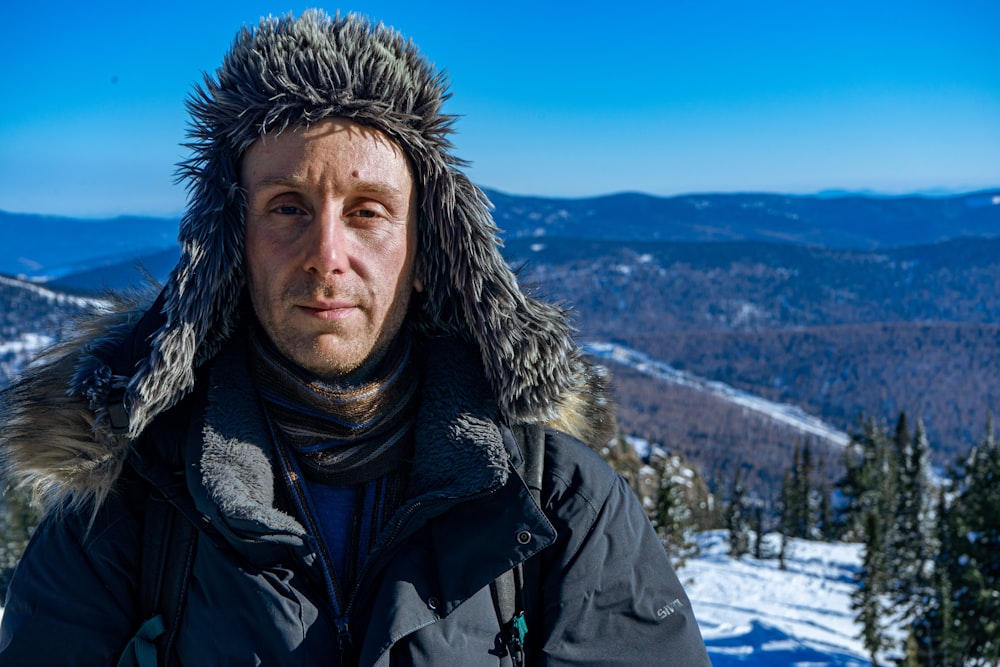 a man wearing a furry hat on top of a snow covered mountain