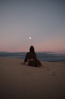 a woman sitting on top of a sandy beach
