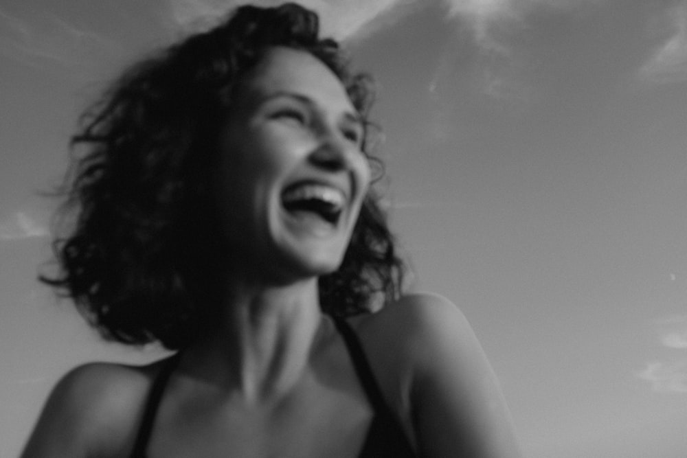a woman laughing while standing in front of a cloudy sky